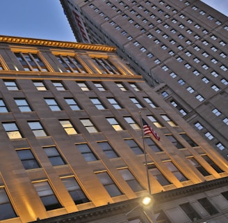 Tall building with illuminated top in blue and red lights, seen from a low angle. The sign 'Horseshoe Casino' is visible near the entrance. An American flag is also visible in the foreground. The building has numerous windows and a street light is present in front of the casino.