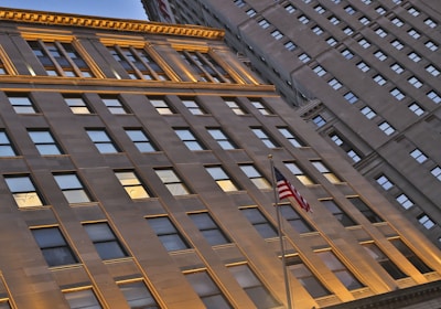 Tall building with illuminated top in blue and red lights, seen from a low angle. The sign 'Horseshoe Casino' is visible near the entrance. An American flag is also visible in the foreground. The building has numerous windows and a street light is present in front of the casino.